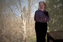 Lonna leans against wall bare limbs and branches projected onto her and wall with camera obscura