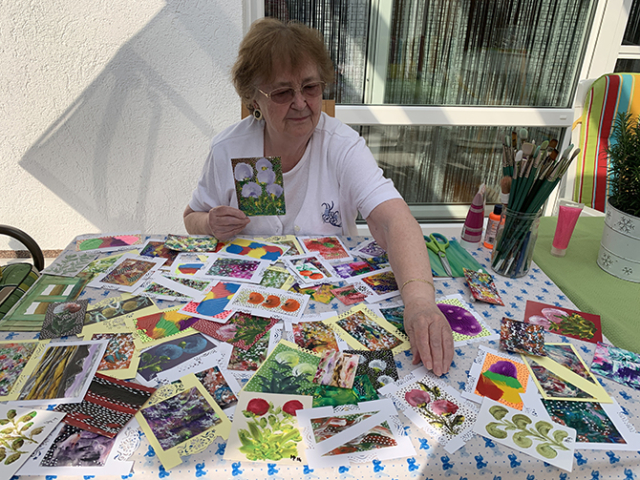 Artist sitting at table filled with small colorful paintings