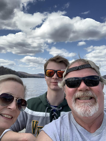 close up of three smiling adults with lake and blue sky in background