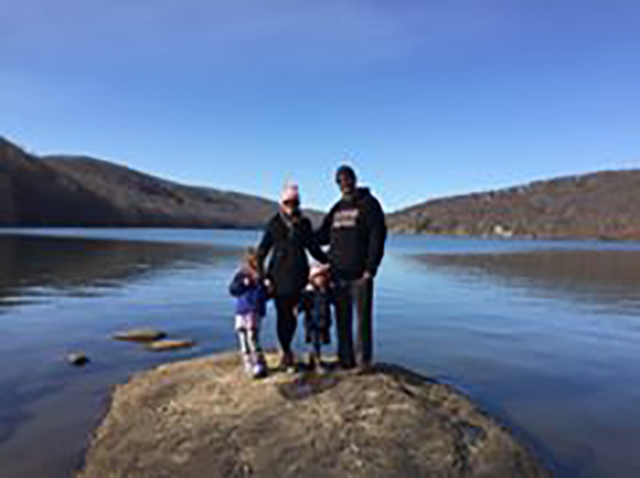 two adults with two children standing on rock with lake and hills in background