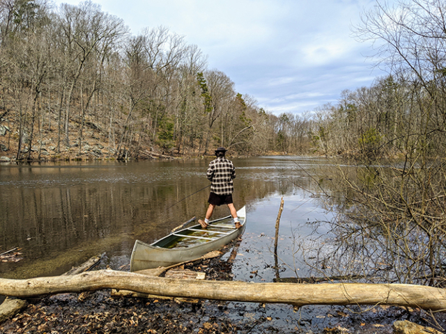 young man standing in beached canoe fishing in lake
