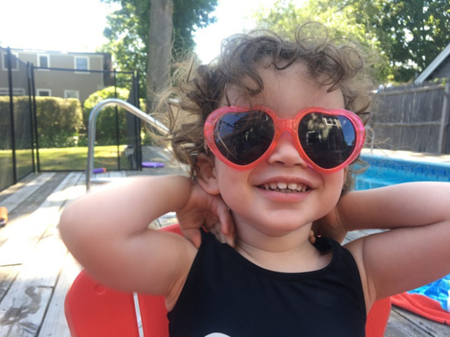 curly haired smiling child with big heart sunglasses