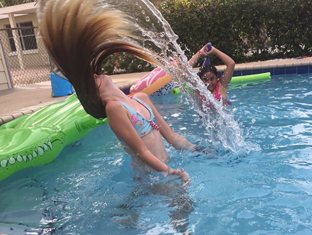 two girls in pool one girl throwing her long hair backward