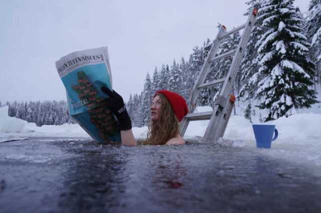 woman in hat and gloves submerged reading newspaper in cold wintry lake